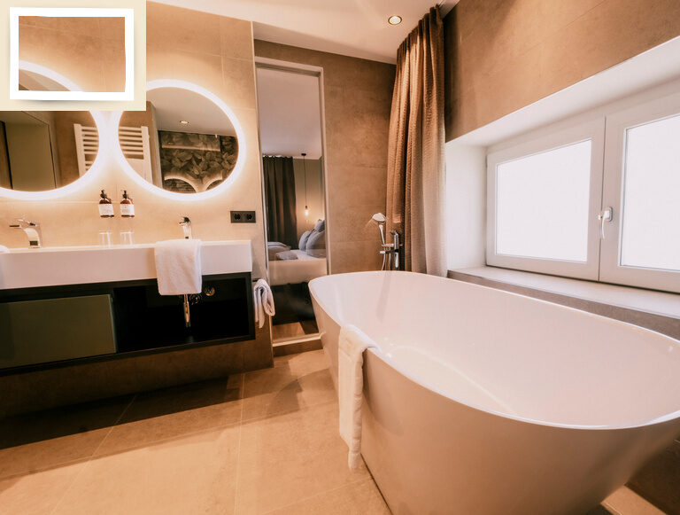 Eine weiße Badewanne steht neben einem Waschbecken im luxuriösen Badezimmer der Hotel Holzapfel Suite Golden Delicious.