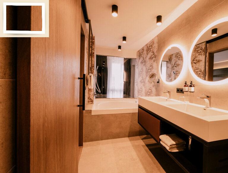 Das elegante Badezimmer in der Suite Goldrenette mit einem großen Spiegel über dem Waschbecken im Wellnesshotel Holzapfel in Bad Füssing.