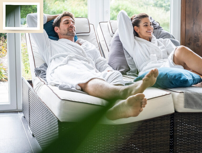 Zwei Personen entspannen sich mit hochgelegten Füßen auf gemütlichen Liegen im Ruhebereich des Thermenhotels Holzapfel in Bad Füssing.