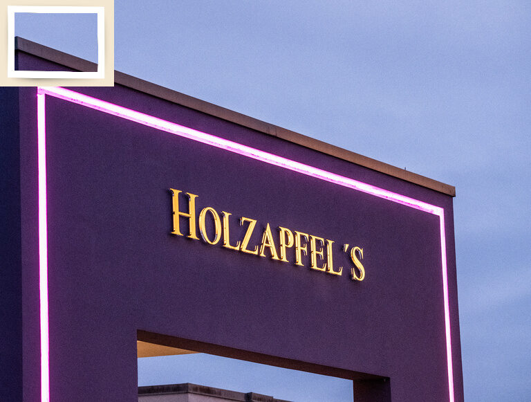 Das 4-Sterne-Hotel Holzapfel in Niederbayern mit auffälligem lilafarbenen Eingangsbogen und beleuchtetem Hotelnamen.
