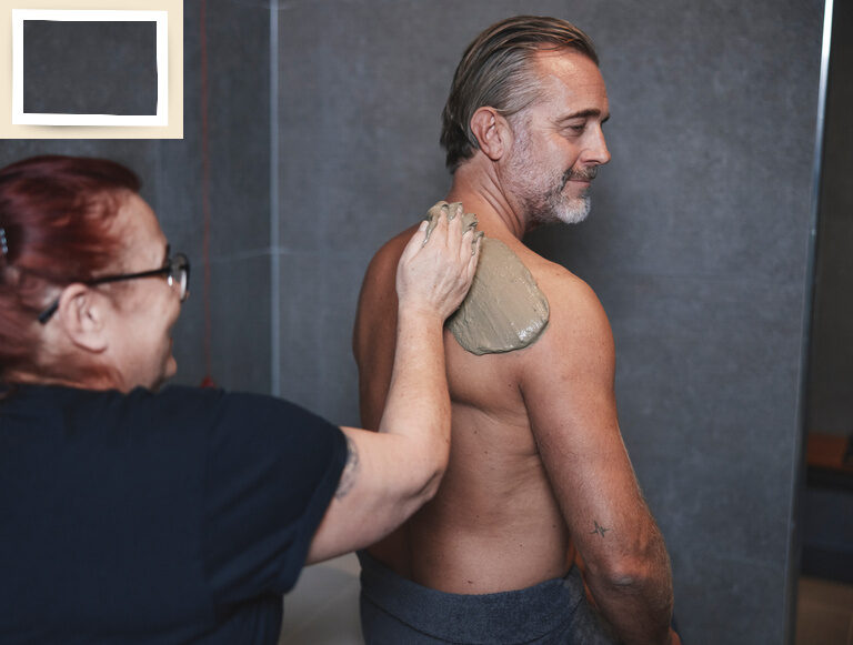 Eine Frau gibt einem Mann eine Wellnessanwendung in Form einer Rückenmassage mit Mineralschlamm im Wellnesshotel Holzapfel im Rottal.