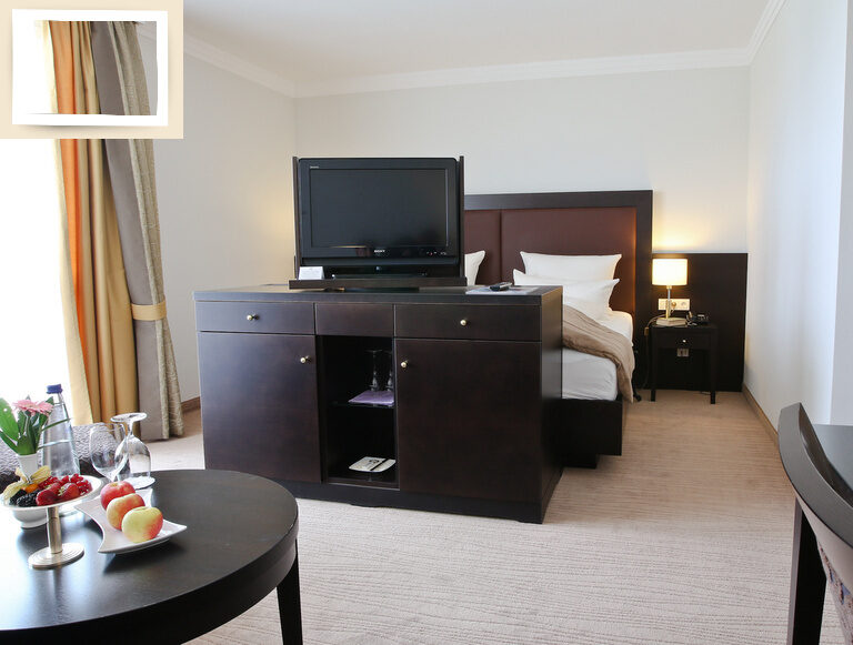 Bequemes Bett und ein Tisch mit Fernseher im Doppelzimmer Deluxe Ost des Wellnesshotel Holzapfel in Bad Füssing.