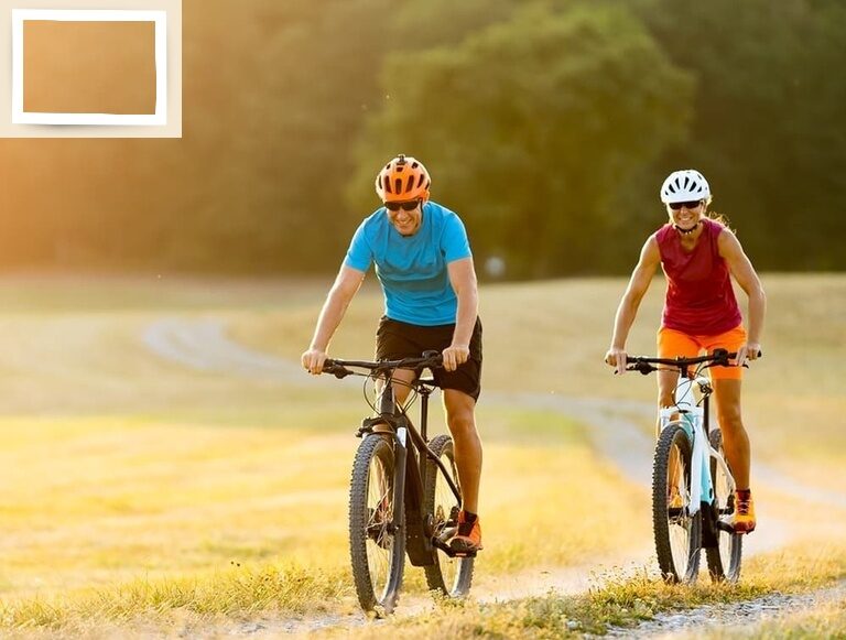 Zwei Personen in sportlicher Kleidung radeln auf einem Feld in Bad Füssing bei Sonnenuntergang.