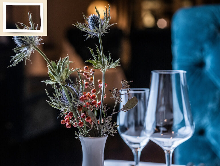Eine elegante Vase mit bunten Blumen und Gläsern als zentrale Tischdekoration im Restaurant Glockenturm des Hotel Oswald bei Passau.