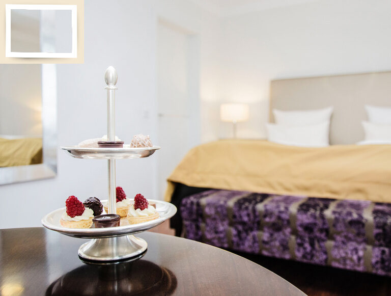 Ein gedeckter Tisch mit einem süßen Dessertteller vor dem Bett in der Gala Suite des Hotel Holzapfels in Niederbayern.
