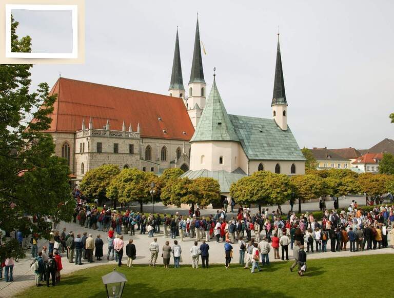 Eine Menschengruppe versammelt sich vor der eindrucksvollen Altöttinger Kirche, einem beliebten Wallfahrtsziel.