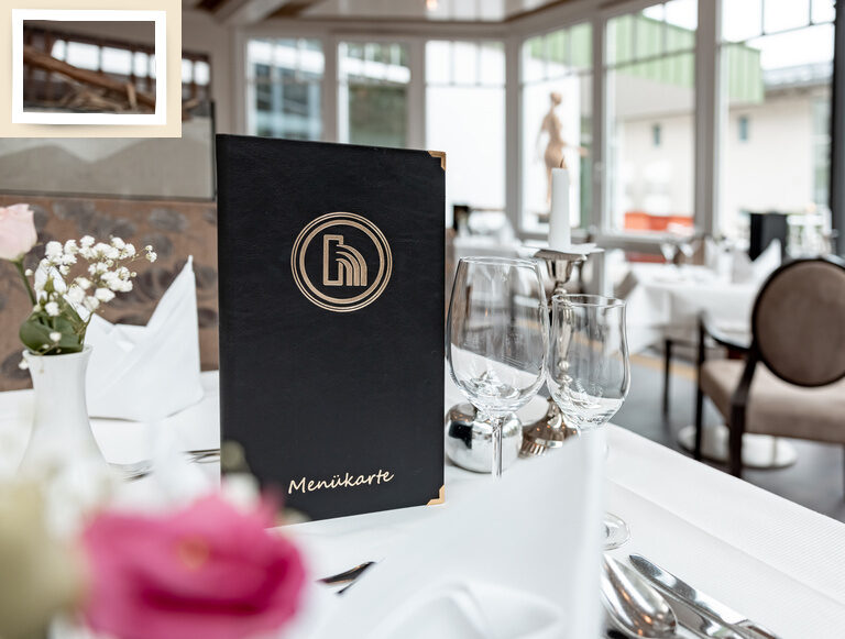 Elegantes Tischdesign mit einer Menükarte und klaren Weingläsern im Wintergarten des Wellnesshotel Holzapfel.