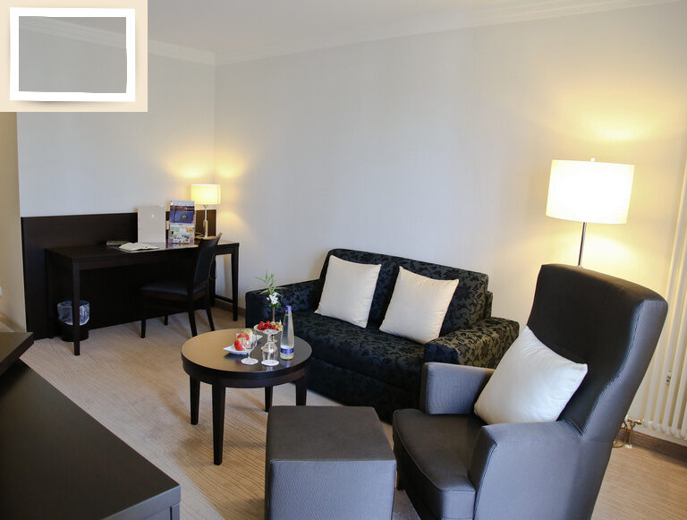 Vielseitig ausgestatteter Wohnbereich des Doppelzimmer Deluxe Ost im Hotel Holzapfel in Bayern mit Schreibtisch, Sitzmöglichkeiten und Fernseher.