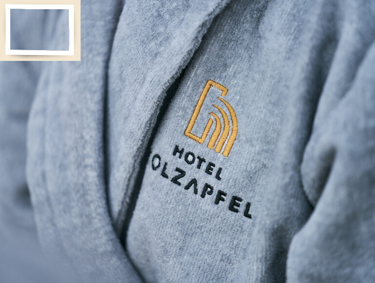 Das stilvolle Wellnesshotel Holzapfel Logo ziert einen flauschigen Bademantel für den Wellnessbereich.