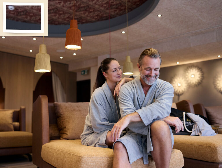 Ein Mann und eine Frau sitzen glücklich auf einem Sofa im Ruhebereich des Gesundheitshotels Holzapfel im Rottal.