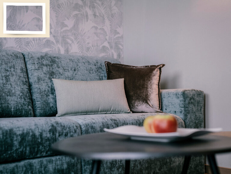 Ein kleiner Sofatisch mit einem Apfel darauf steht vor einer gemütlichen Couch im Doppelzimmer Comfort des Tagungshotels Holzapfels in Niederbayern.