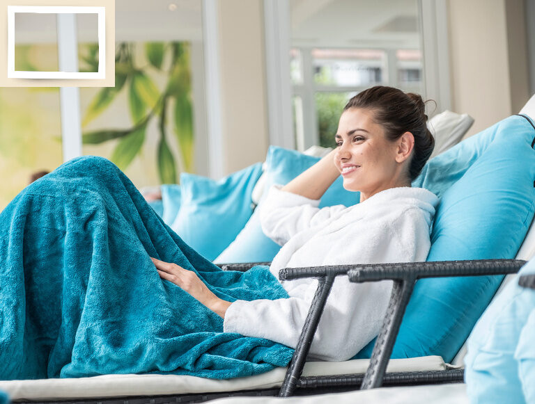 Eine Frau liegt auf einer Liege im Ruhebereich des Wellnesshotels Holzapfels, gemütlich eingehüllt in einer blaue Decke.
