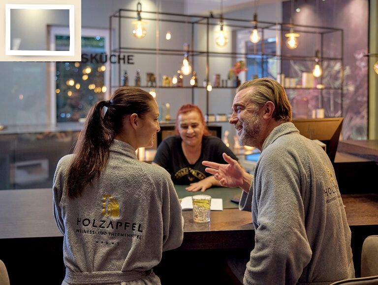 Zwei Personen führen ein Gespräch mit einer Mitarbeitern zu einem Angebot des Spa Bereichs im Hotel Holzapfe
